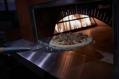 Pizza being prepared in a wood-fired oven