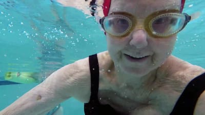 A senior woman swimming underwater in a pool
