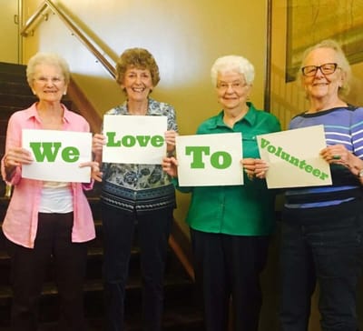 Four residents holding signs saying 'We Love To Volunteer'
