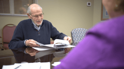 An elderly man reading documents with a visitor