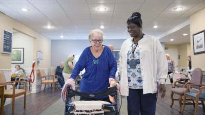 Resident using a walker with staff assistance in an activity area