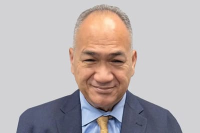 A man in a suit smiling against a grey background