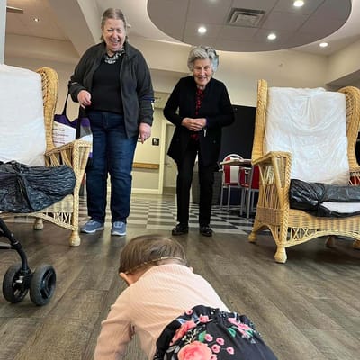 Two smiling women interacting with a crawling child in a common area