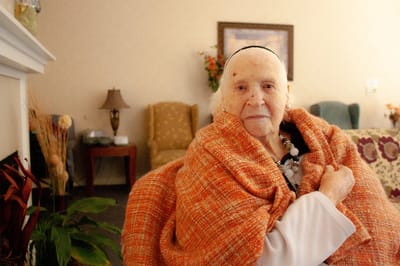 An elderly woman wrapped in a cozy blanket indoors.