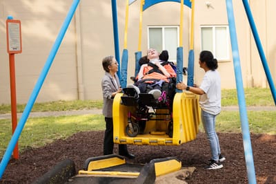 Residents enjoying adapted swing with staff assistance.