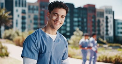 Healthcare worker smiling outdoors with colleagues in background.