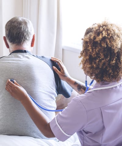 Nurse with stethoscope attending to patient in bed.
