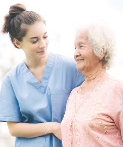 Healthcare worker assisting an elderly woman outside.