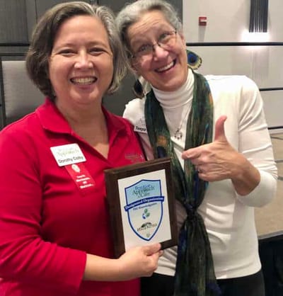 Two women celebrating with an award plaque.