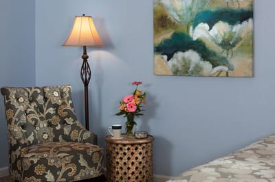 Cozy corner with a chair, lamp, and flowers in a resident room
