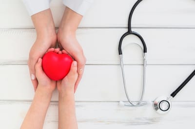 Hands holding a red heart and stethoscope on a table