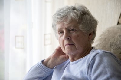 Senior woman sitting indoors, looking thoughtfully.