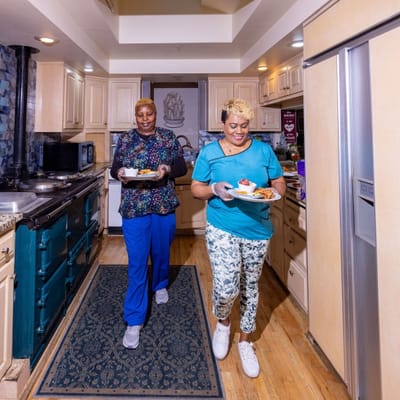 Two staff members serving food in a kitchen