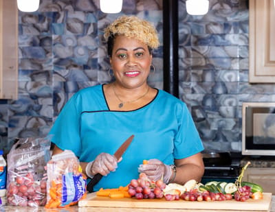 Staff member preparing fresh fruits and vegetables in the kitchen.