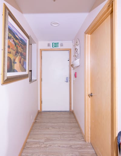 A hallway with a door, artwork, and exit sign
