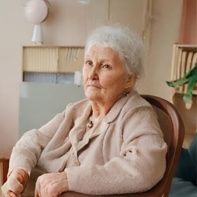 An elderly woman sitting in a comfortable chair in an interior setting