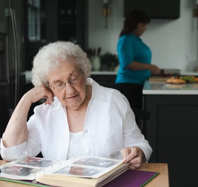 Elderly woman looking at a photo album with a caregiver in the background