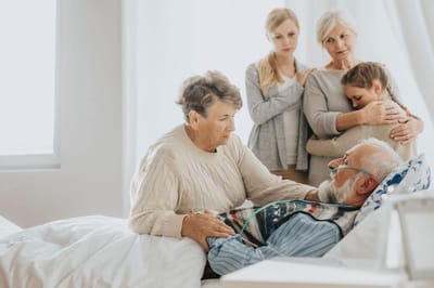 Family visiting an elderly man in a hospital bed.