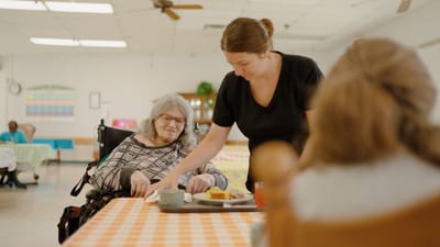 Staff serving food to a resident in a dining room.