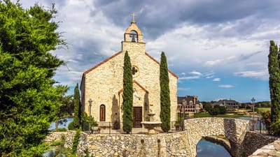 Exterior view of a stone church with cypress trees