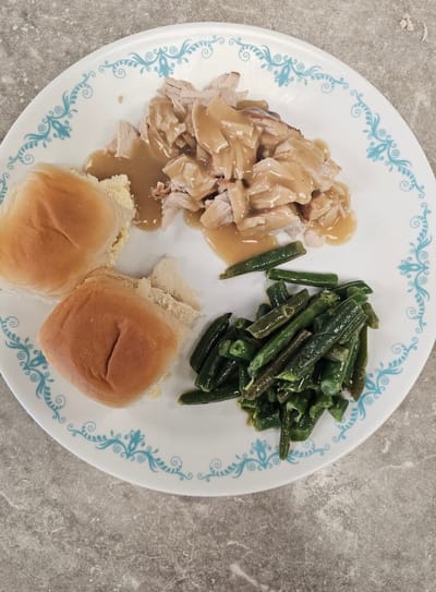 A plate of food including turkey, green beans, and bread rolls