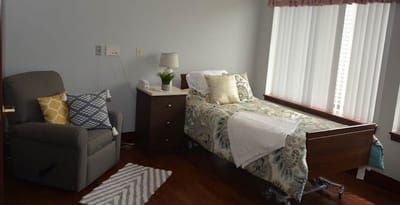 A cozy private resident room with a bed and chair