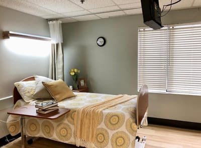 A well-decorated resident bedroom with a bed, bedside table, and natural light.