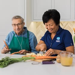 A senior man and a caregiver preparing vegetables together in a bright kitchen.