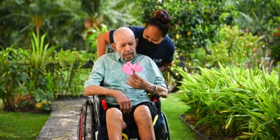 Resident enjoying a flower with staff assistance in a garden