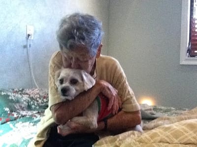 An older resident cuddling a small dog in a room