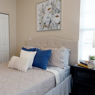 A cozy resident room with a neatly made bed and decorative pillows.