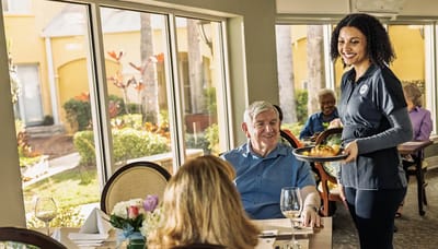 A staff member serving food to residents in a dining area