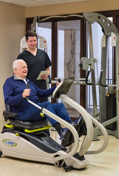 Senior man exercising with staff assistance in gym.