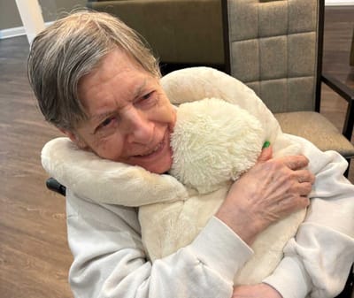 Resident hugging a stuffed animal in a cozy setting.