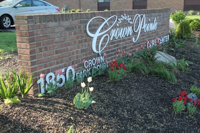 Exterior sign for Crown Pointe Care Center surrounded by flowers