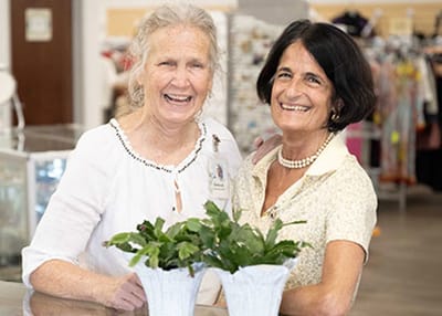 Two smiling women posing with potted plants in a common area