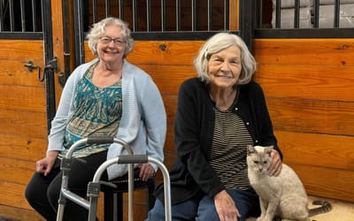 Two senior women smiling with a cat in a cozy setting