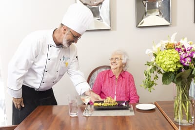 Chef serving a meal to a smiling resident