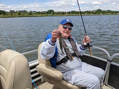 Resident fishing by a lake, smiling with his catch.