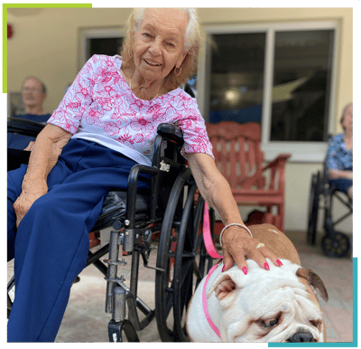 Resident in wheelchair petting a dog outdoors