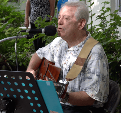 Senior resident playing guitar in a garden area.