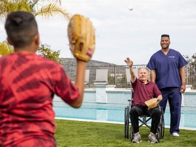 A staff member helping a resident enjoy outdoor baseball.