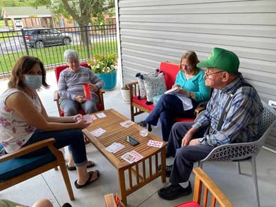 Residents playing cards on a patio with a caregiver