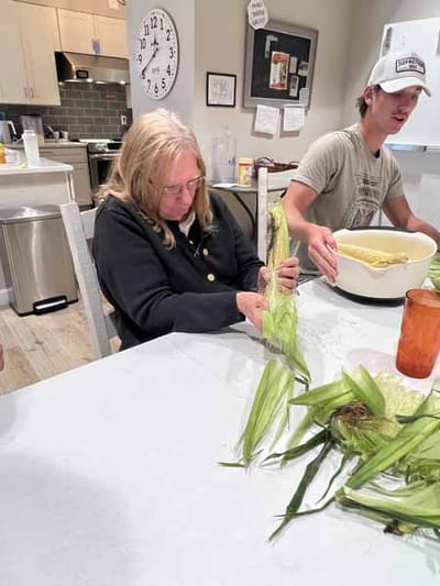 A resident preparing corn with a staff member in a kitchen.