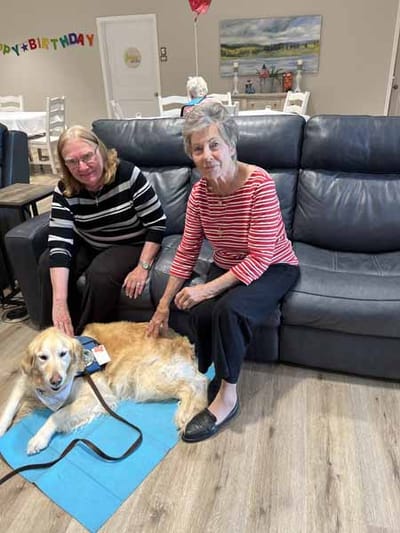 Two residents with a therapy dog in the common area