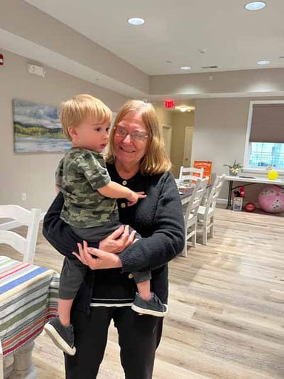 An elderly woman holds a young child in a common area