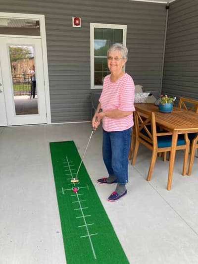 Resident enjoying indoor putting activity on a green mat