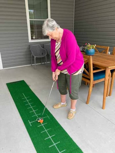 Resident practicing putting on a green mat outdoors