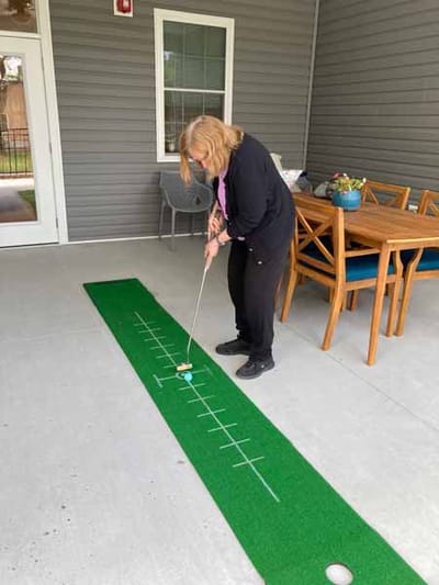 Resident practicing putting on a green mat outdoors