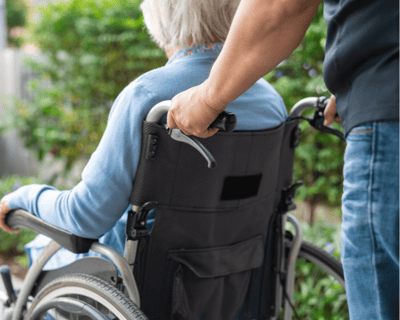 A caregiver pushing a resident in a wheelchair outdoors.